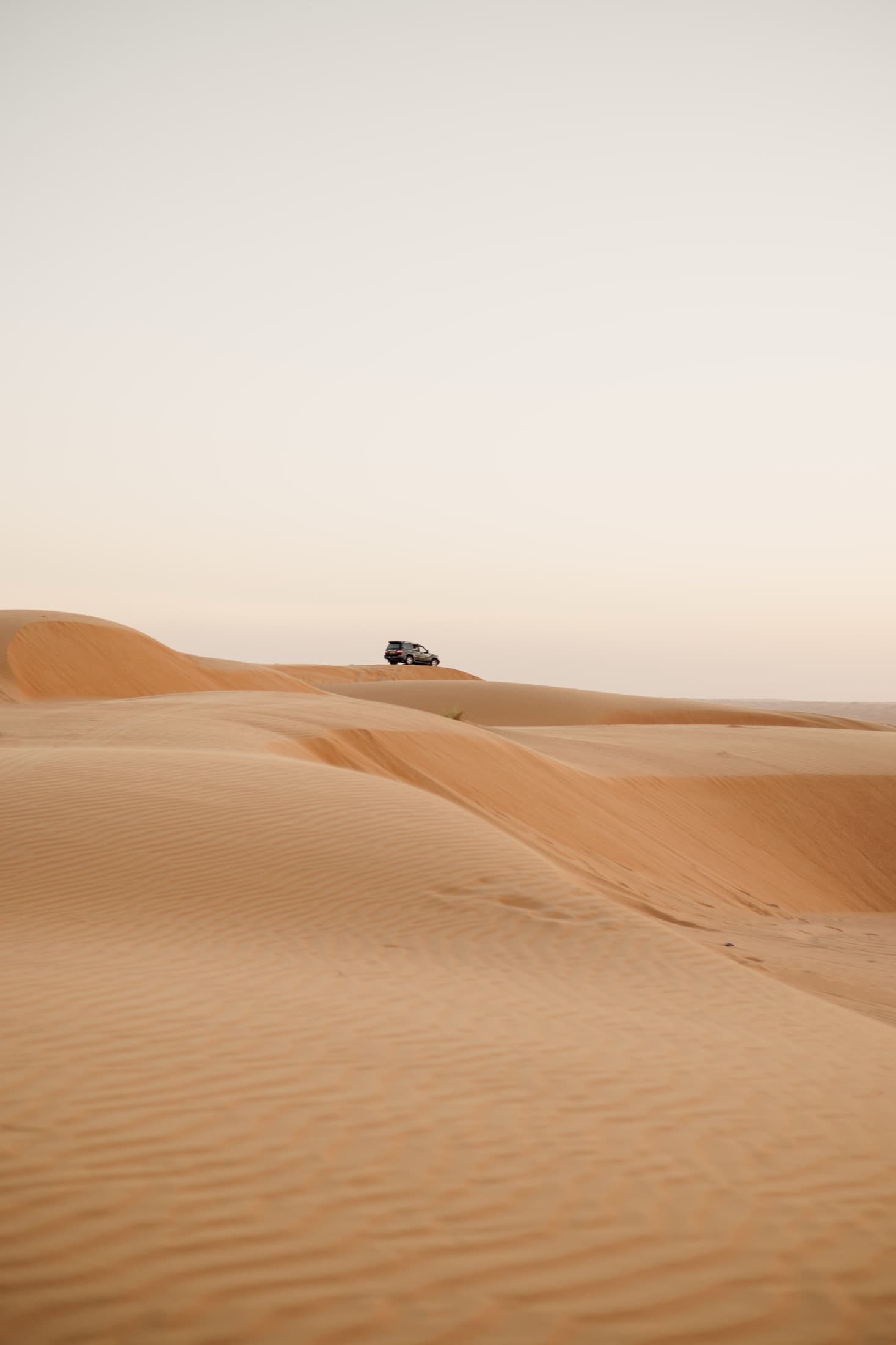 A lone SUV driving over the vast red sand dunes of the Dubai desert
