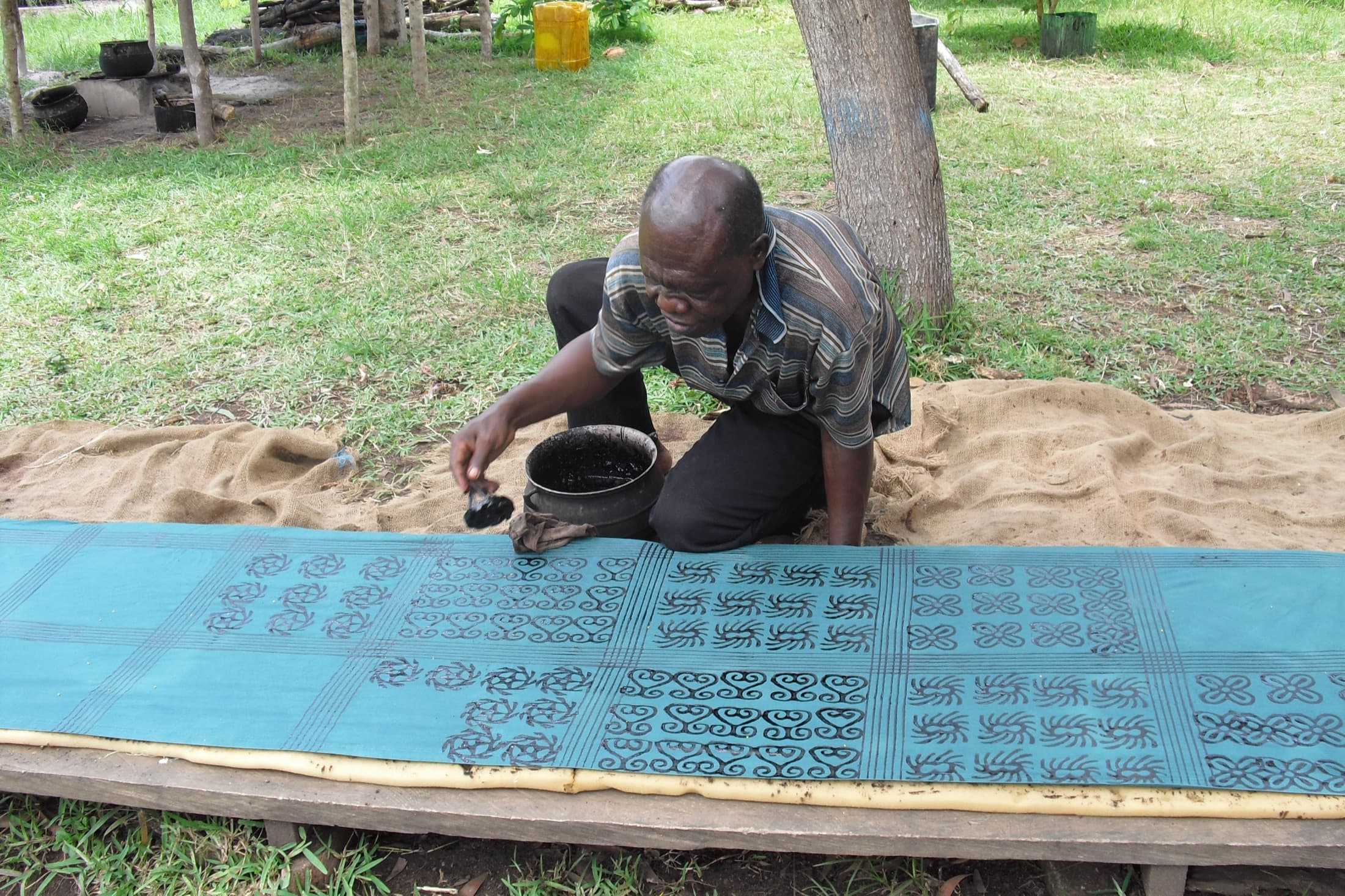A craftsman stamping traditional Adinkra symbols onto cloth with a calabash stamp in Ntonso