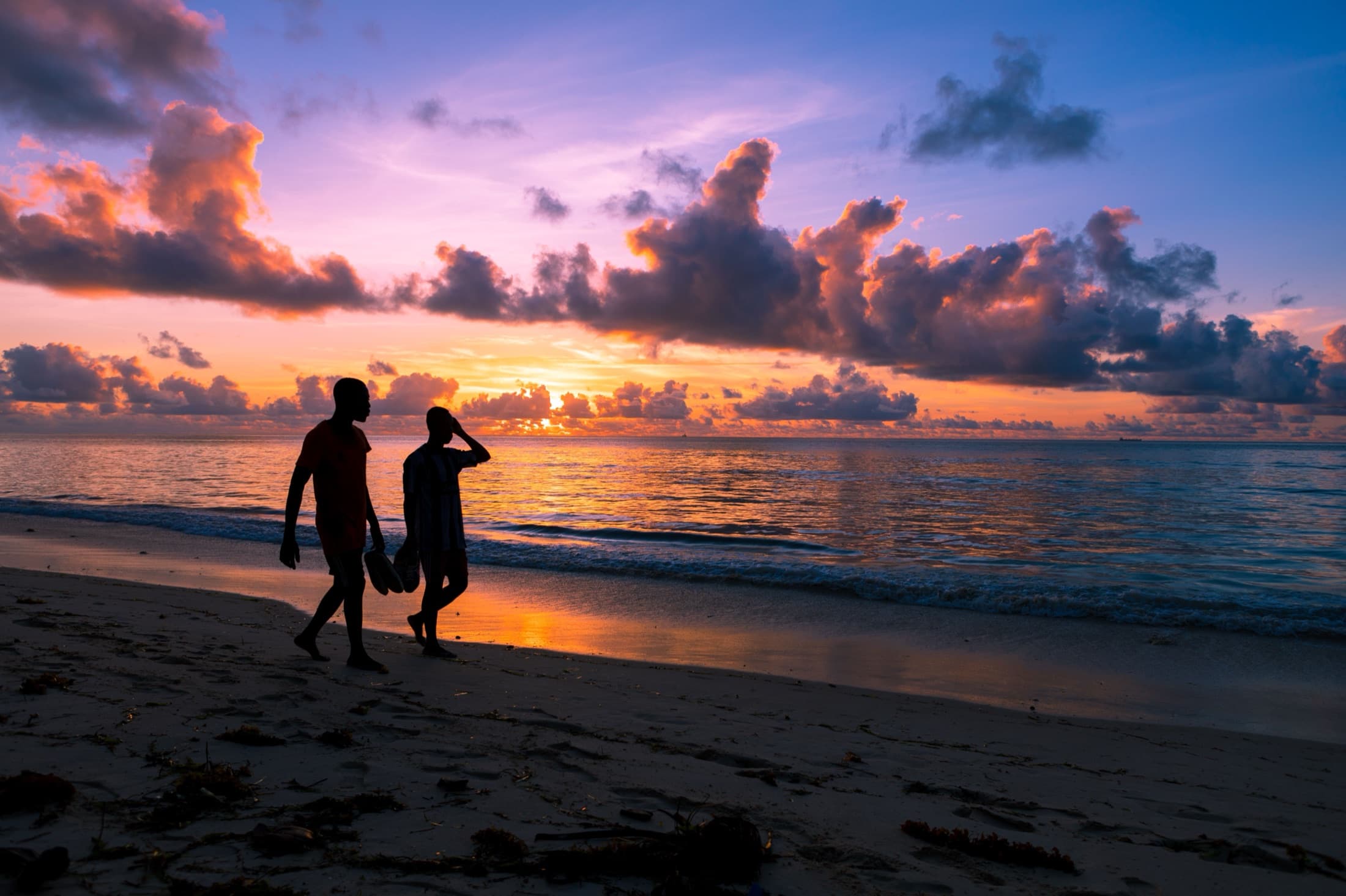 Silhouettes of people walking along Mombasa beach, Kenya during a stunning sunrise