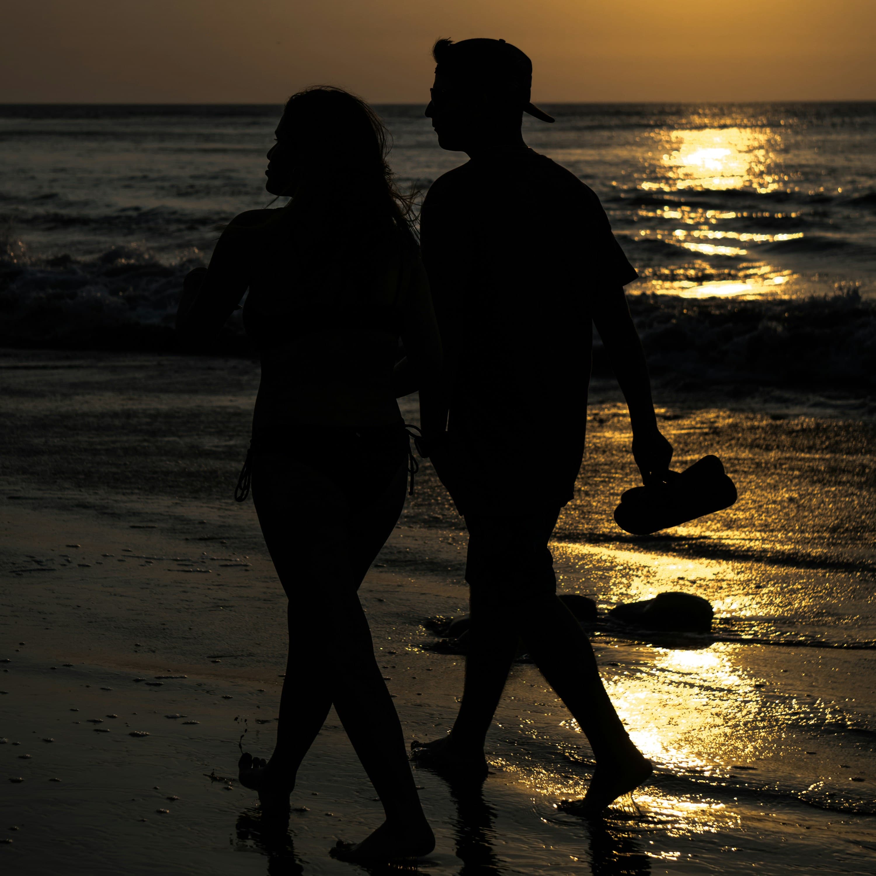 Silhouette of a couple walking together along the shore at sunset